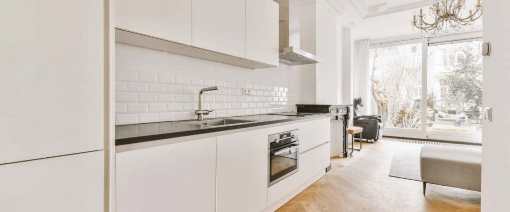 modern, minimalist white kitchen with black countertops, subway tile backsplash, and an open layout leading to a bright living space