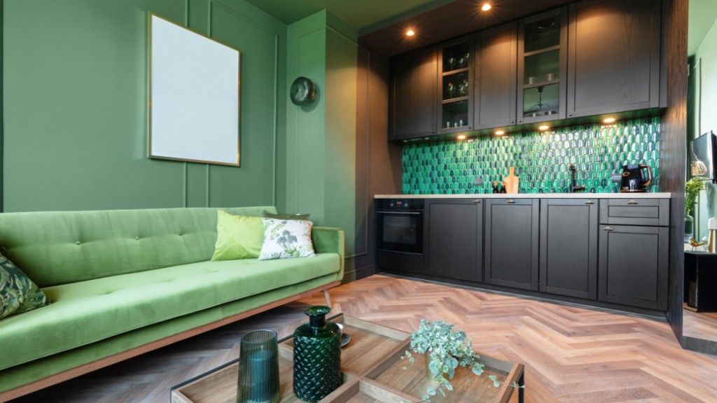 Green living room with dark kitchen cabinets and herringbone floor.