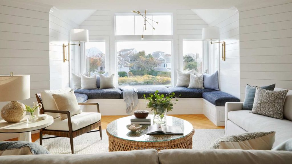 Bright living room with large windows, daylight streaming in, backless couches with cushions, and a side table lamp