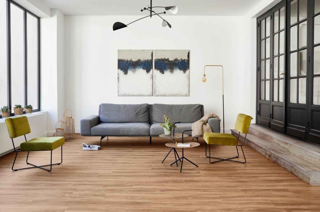 living room with a wooden floor mat, grey couch, two small tables, and two chairs