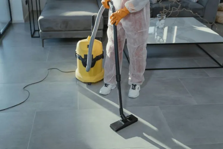 professional cleaner in protective gear vacuums a modern living room with a wet-dry vacuum, ensuring a spotless tiled floor.