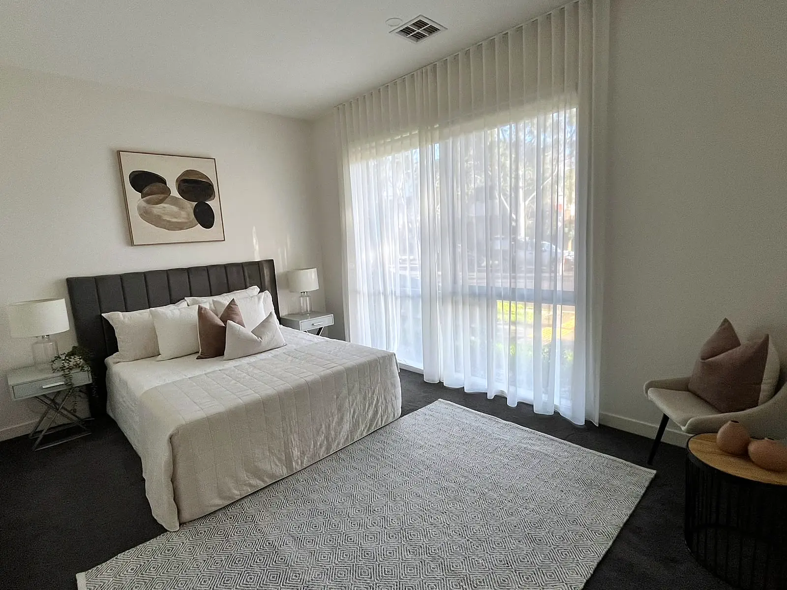 Main bedroom staged with neutral linen and armchair in a Bundoora home