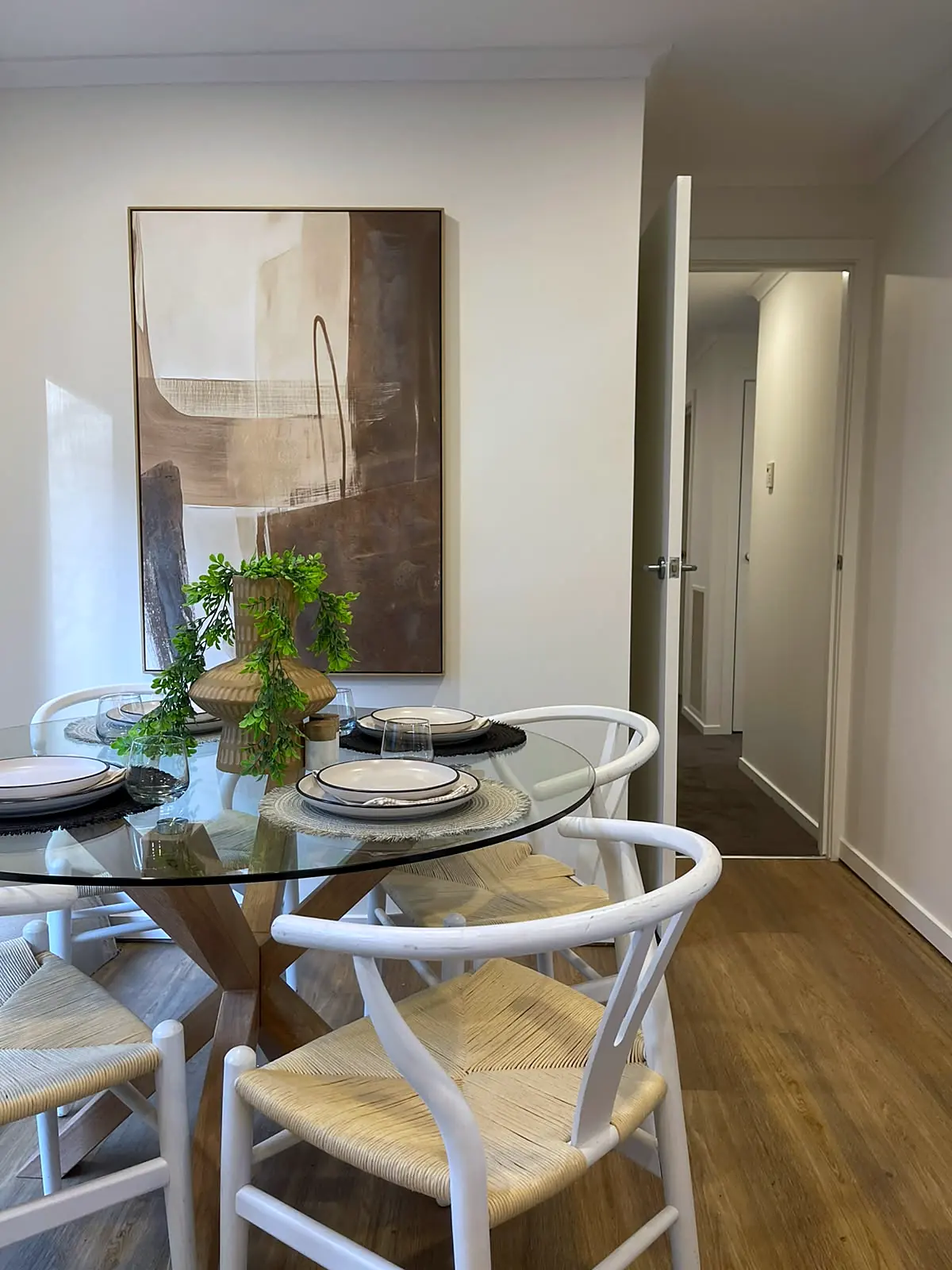 Round glass dining table with white wishbone chairs in a staged Eltham unit