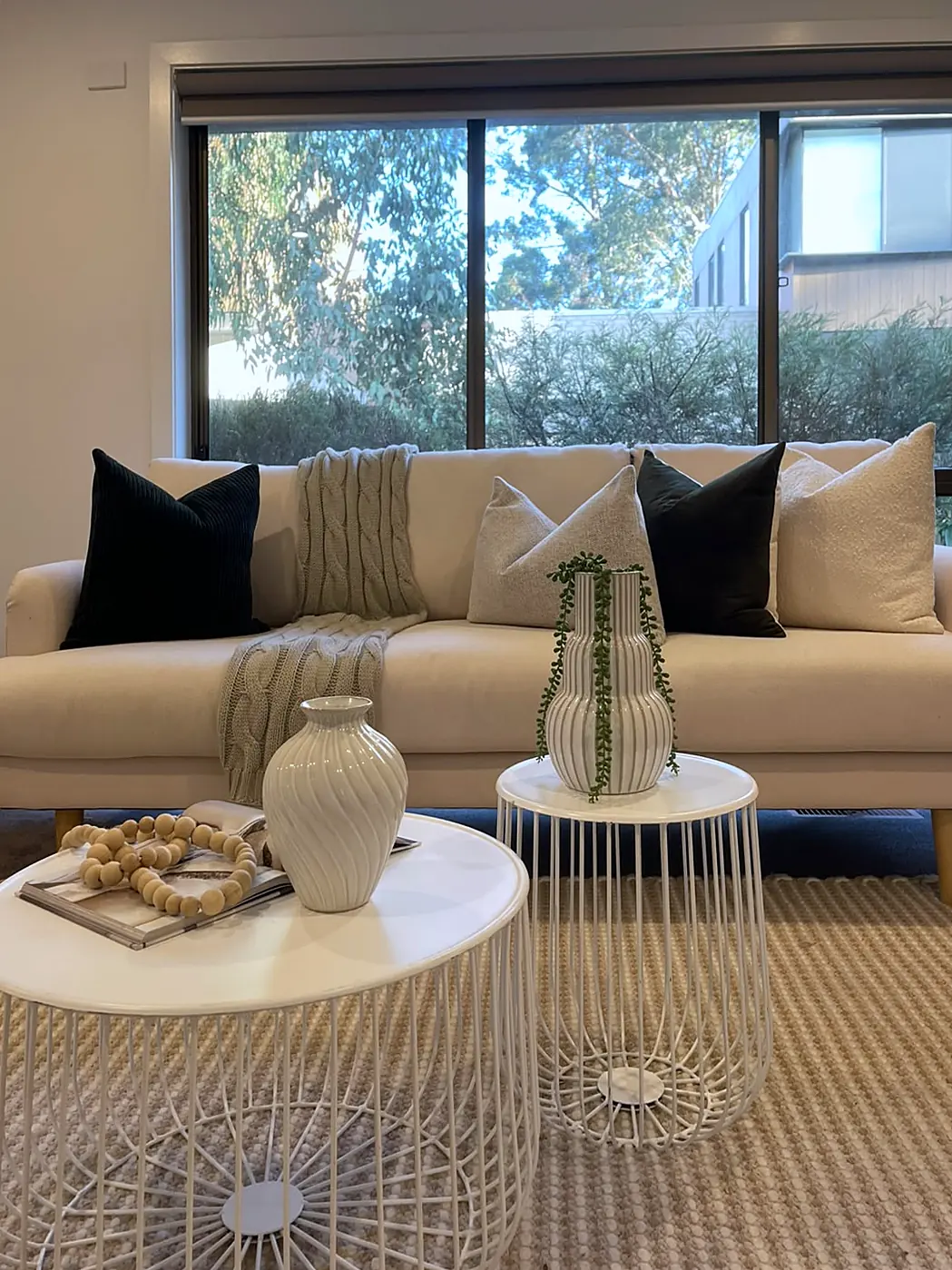 Cream sofa with black cushions beside a window onto the trees in a staged Eltham unit