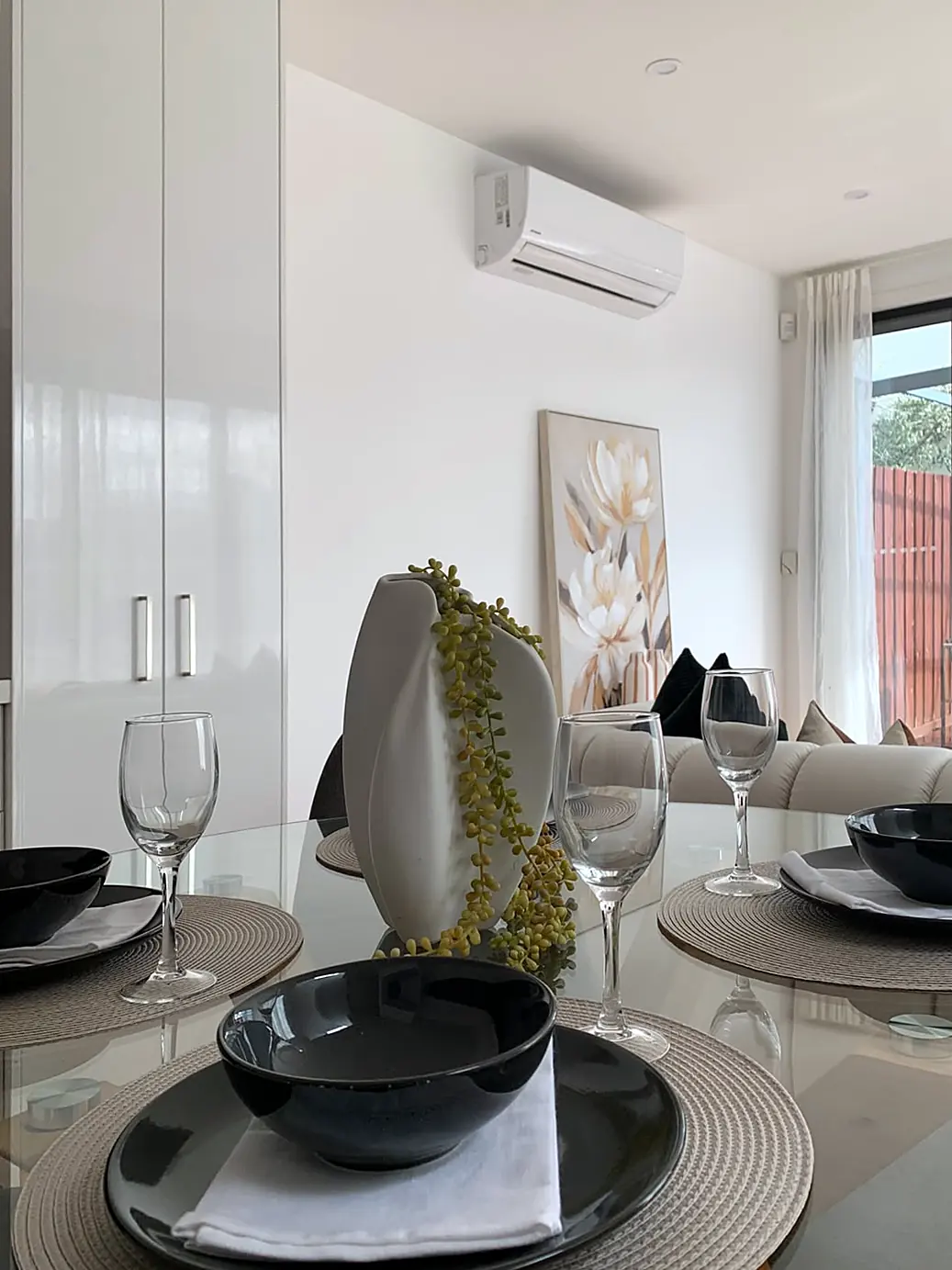 Glass dining table set for four with the living room beyond in a staged Footscray townhouse