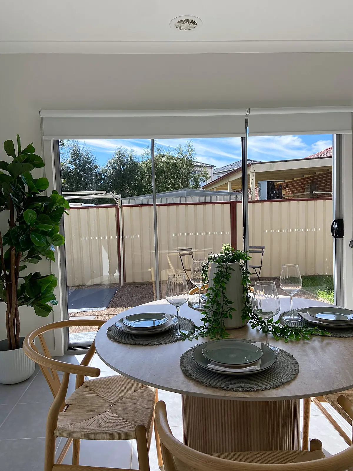 Round timber dining table with wishbone chairs beside sliding doors in a staged Harkness home