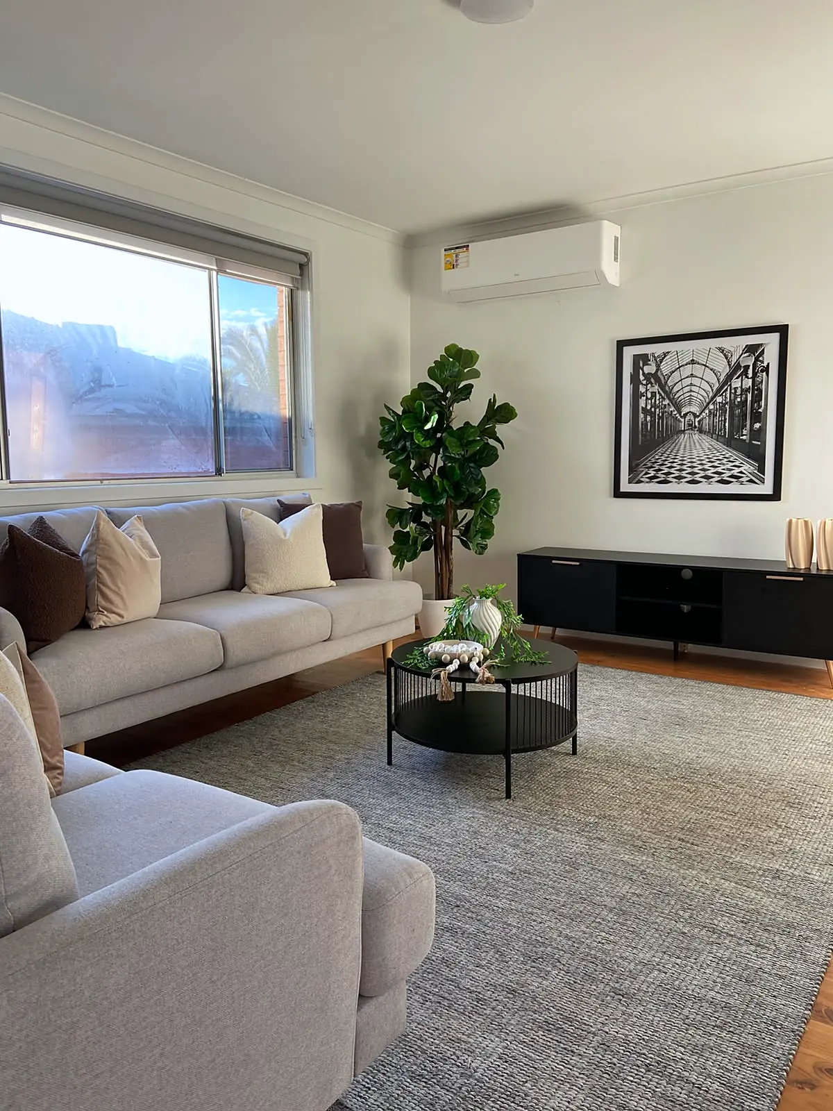 Living room with sofas, black TV unit and tall plant in a staged Lalor unit