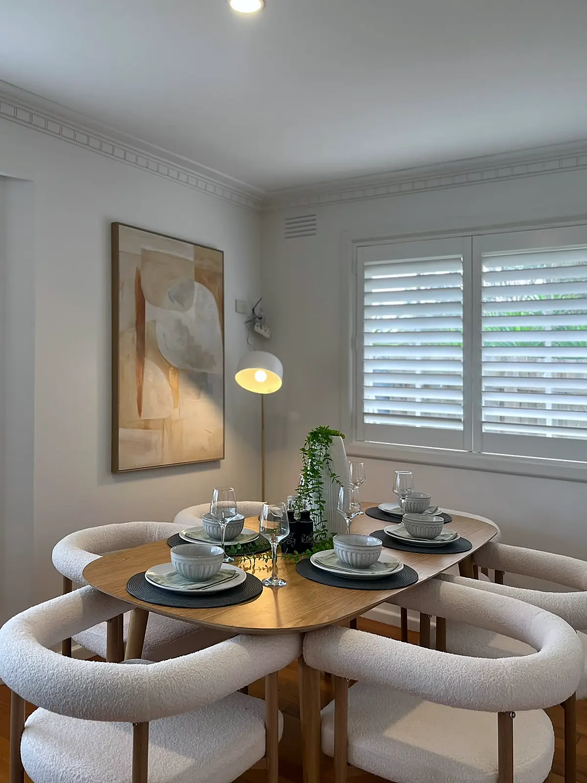 Round timber dining table with boucle chairs beside plantation shutters in a staged Seaholme home