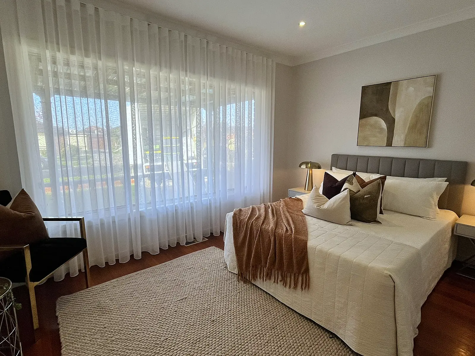 Main bedroom staged with rust throw and armchair in a Sunshine home