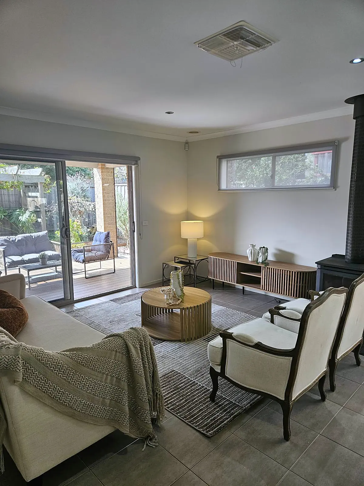Family room with armchairs and wood heater opening to the outdoor area in a staged Taylors Hill home