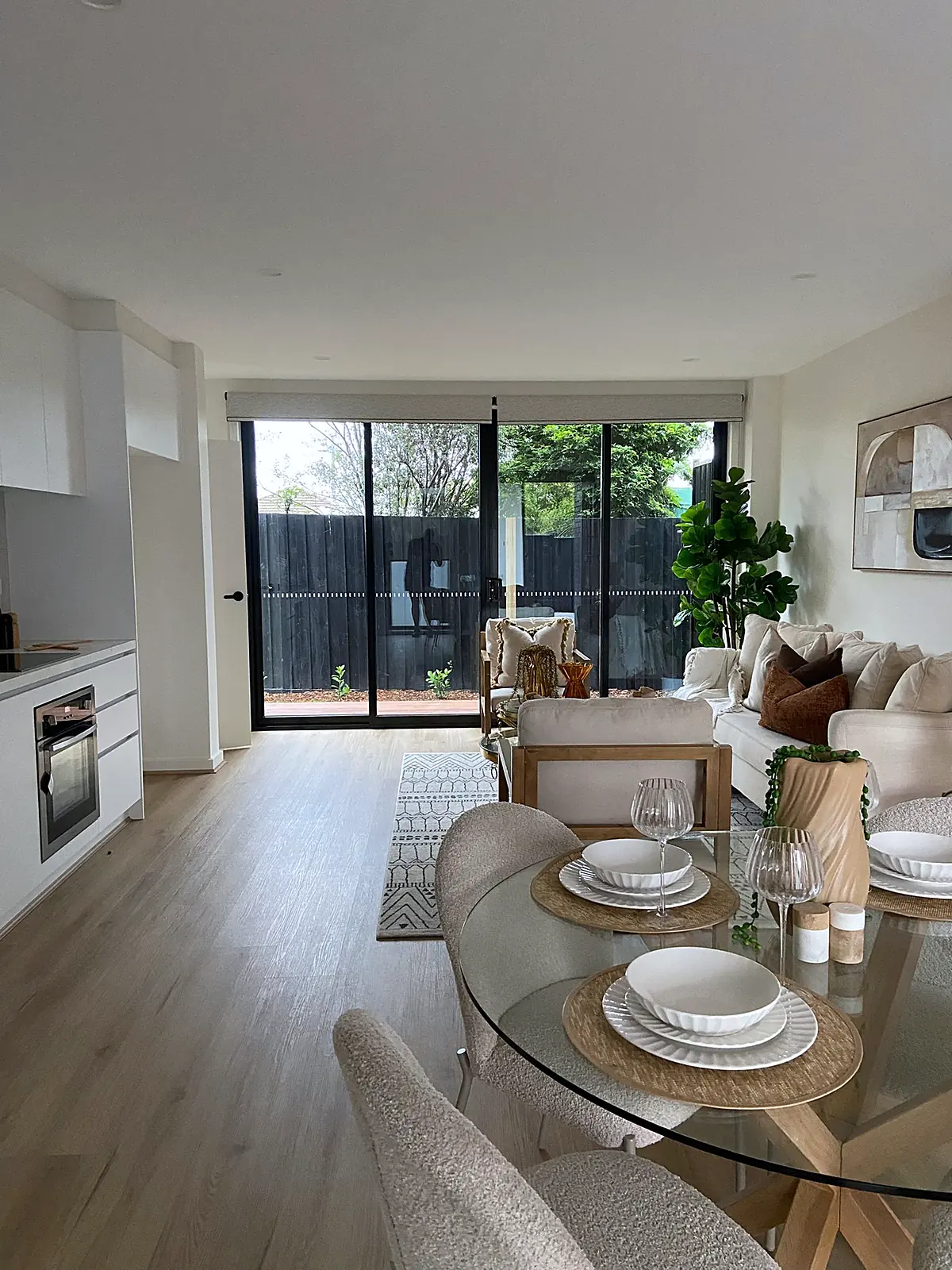 Open-plan dining and living area with glass dining table in a staged Thomastown townhouse
