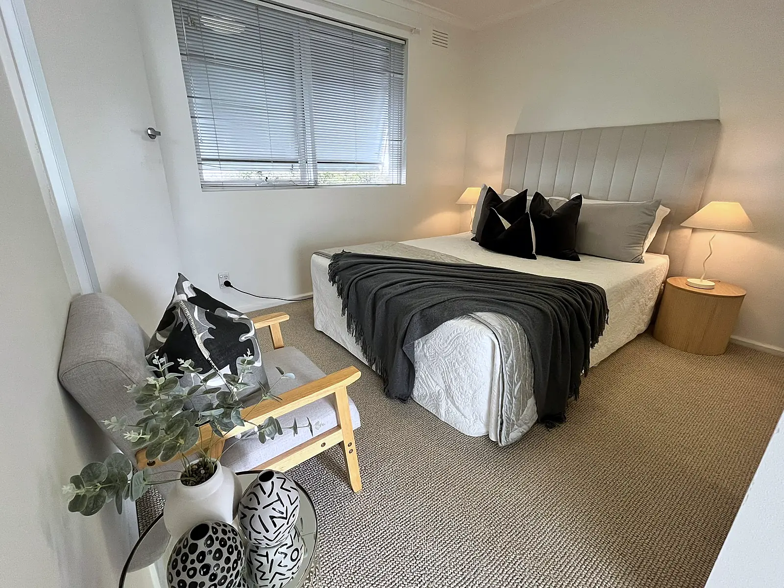 Bedroom staged with upholstered bedhead, charcoal throw and armchair in a Thornbury unit