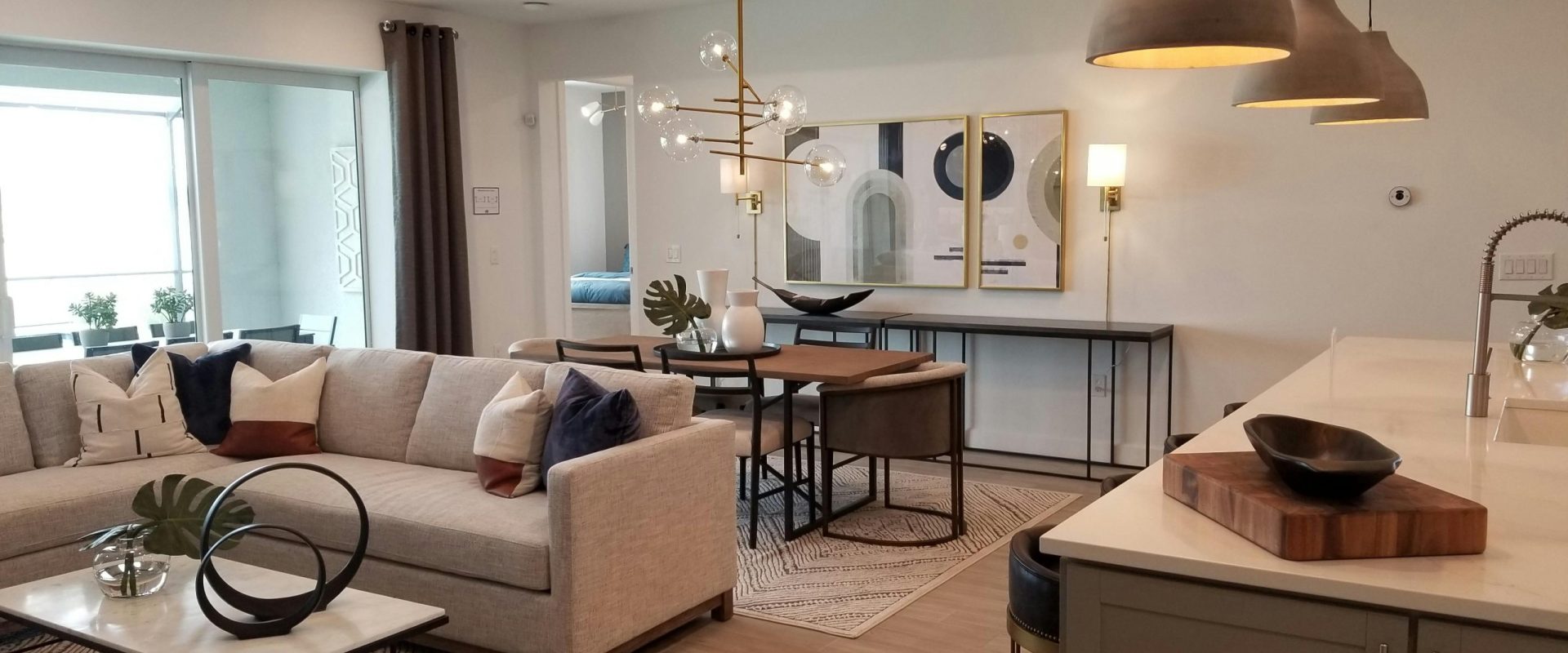 Modern open living area with neutral sectional sofa, chic decor, pendant lighting, and a stylish dining and kitchen space.